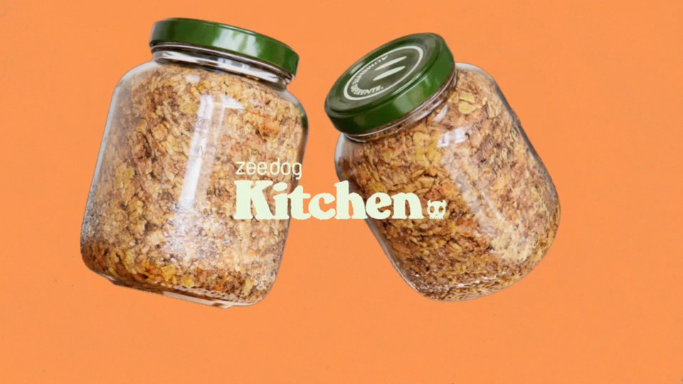 Two Zee.Dog Kitchen food jars with green lids on an orange background.